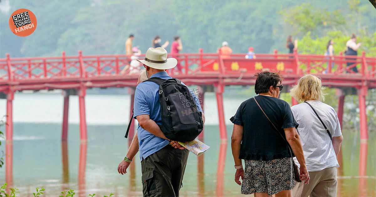 Visitors walking toward the red Huc Bridge at Hoan Kiem Lake, Hanoi